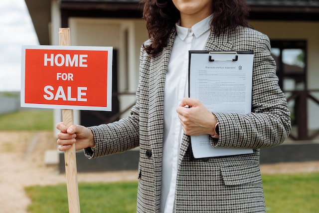 Real estate agent holding a red home for sale sign in front of a house